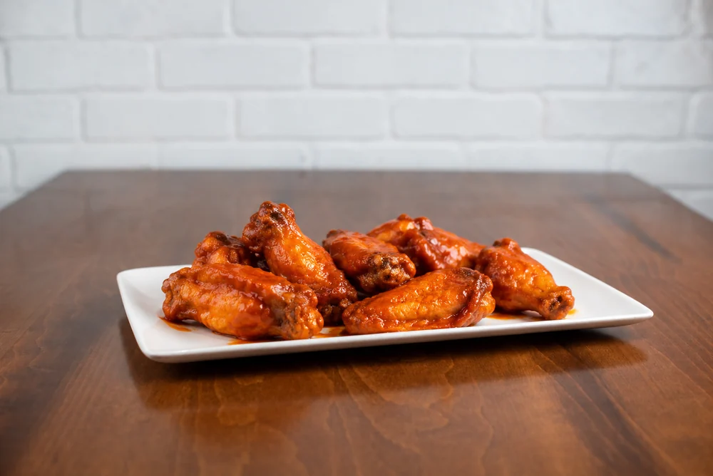 Bone-in wings coated in Buffalo sauce on a white platter